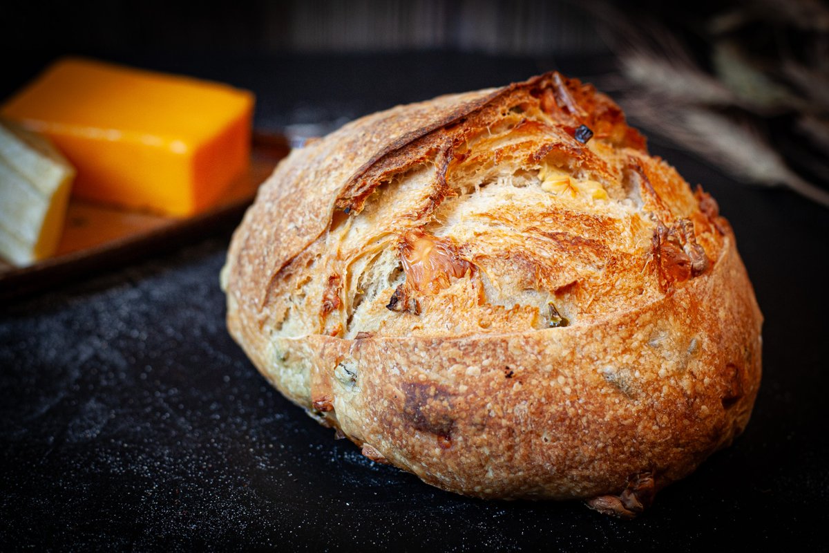 Artisan Jalapeño Cheddar Sourdough loaf with a golden crust and visible jalapeño and cheddar pieces.